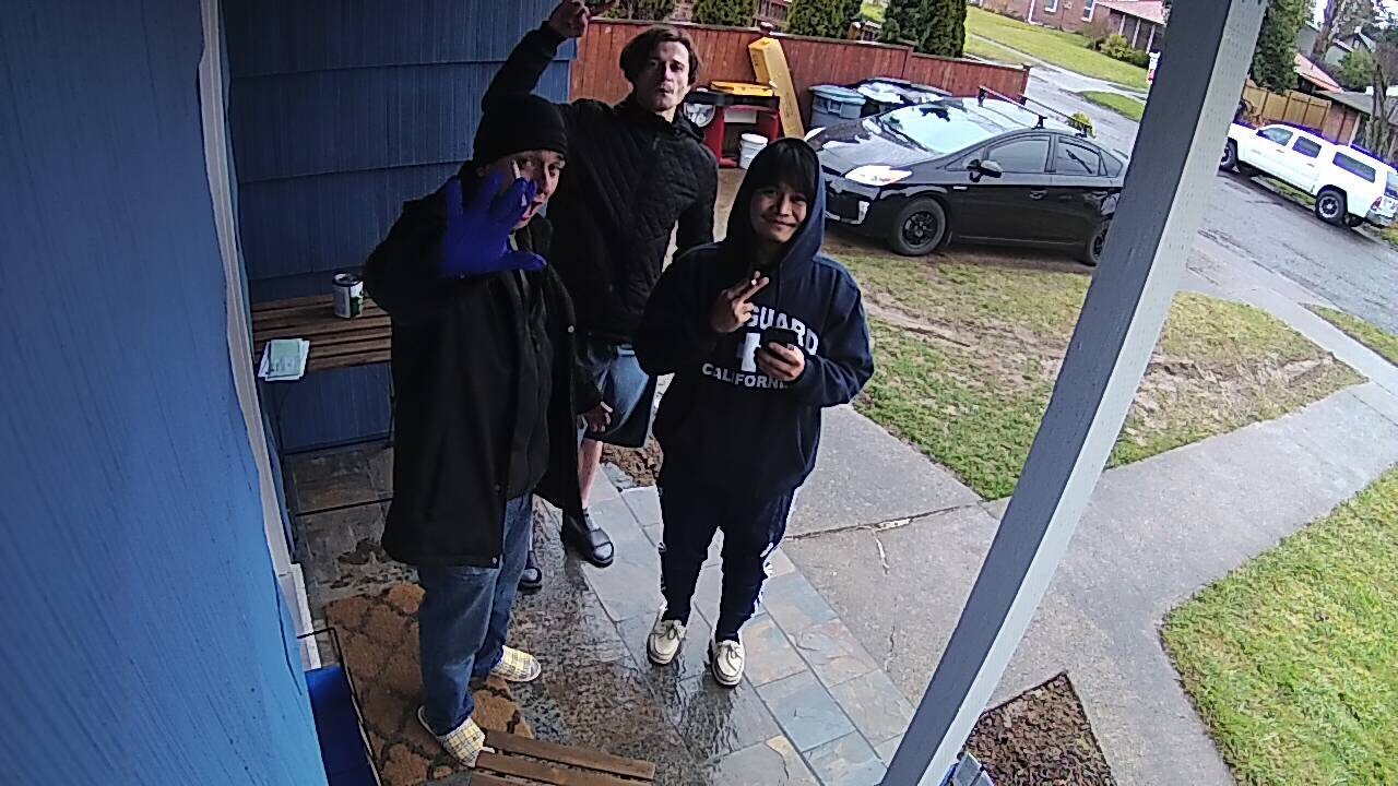 Doorbell-camera still of three people on a front porch on a wet day.